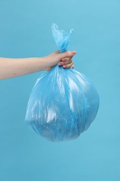 Photo of Woman holding plastic bag full of garbage on light blue background, closeup