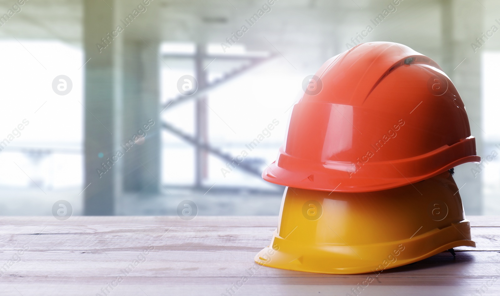 Image of Hard hats on white wooden surface at construction site with unfinished building. Space for text 