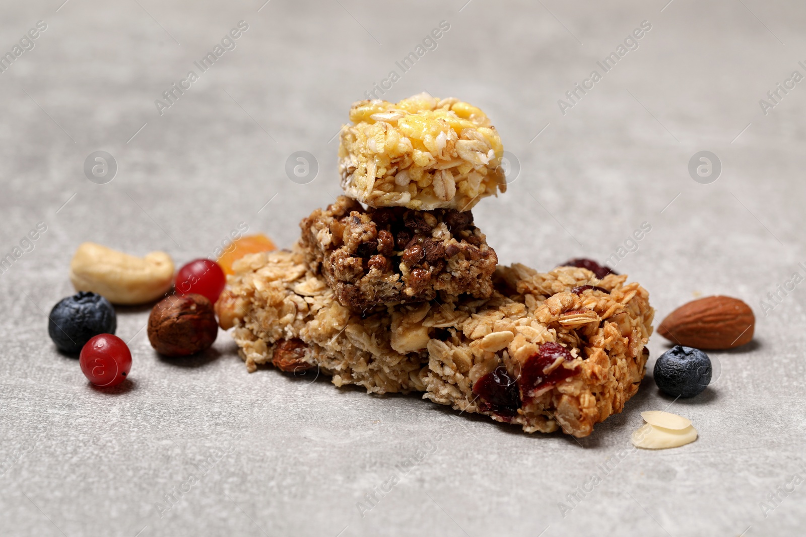 Photo of Tasty granola bars and ingredients on light grey table, closeup