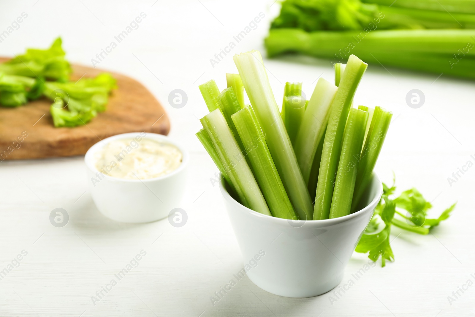 Photo of Celery sticks with dip sauce on white wooden table. Space for text
