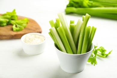 Celery sticks with dip sauce on white wooden table. Space for text