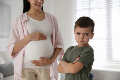 Photo of Unhappy little boy near pregnant mother at home. Feeling jealous towards unborn sibling