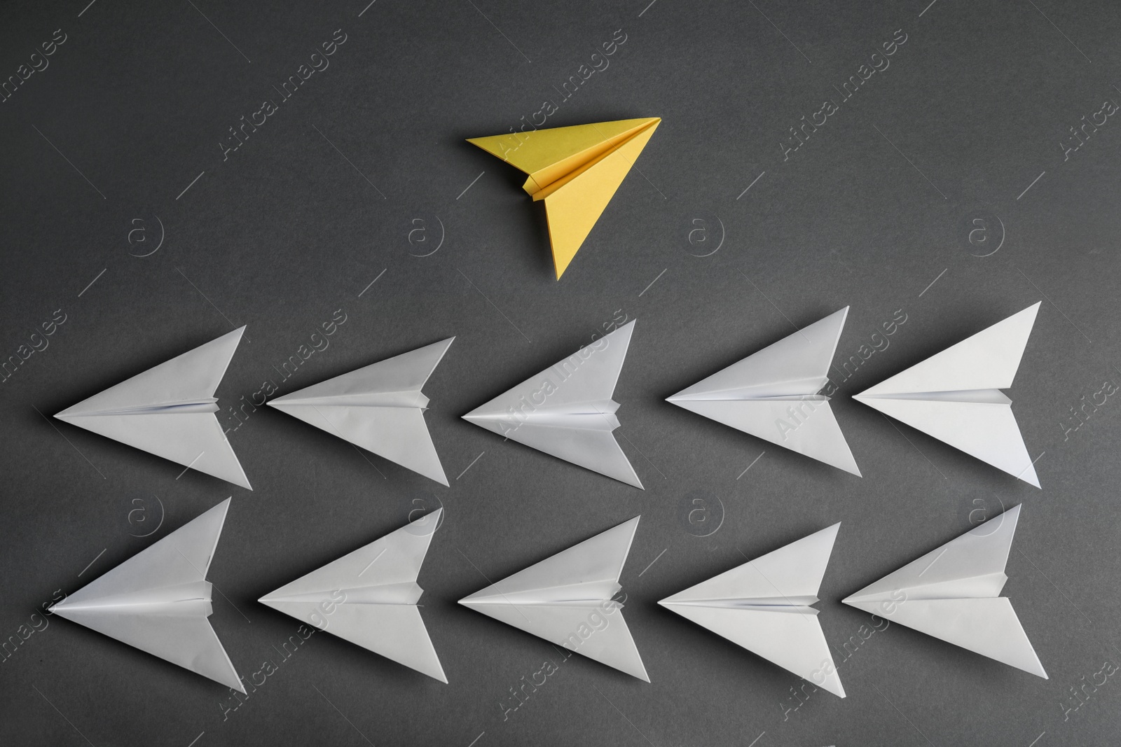 Photo of Different color paper plane flying away from others on dark background, top view