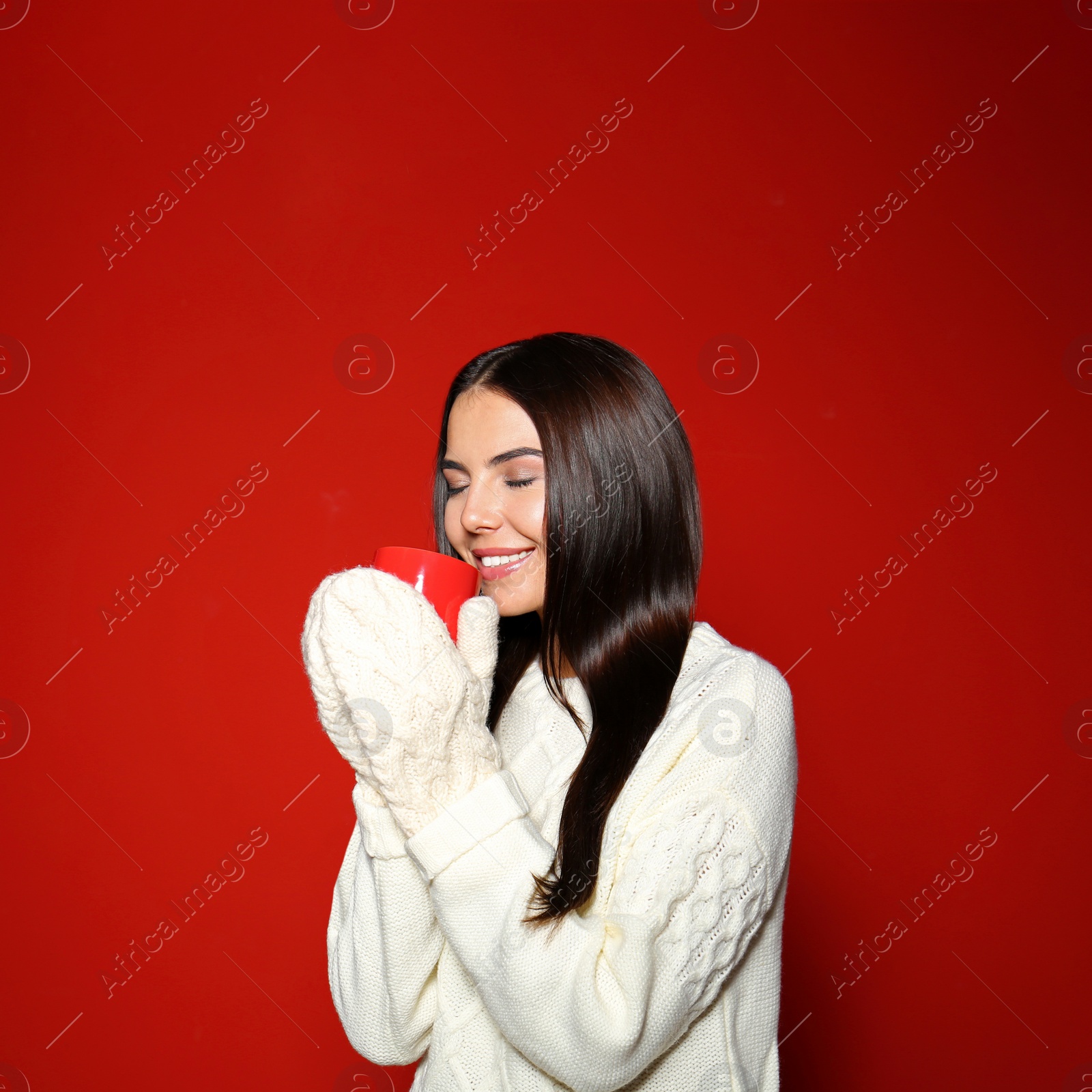 Photo of Young woman in warm sweater with cup of hot drink on red background