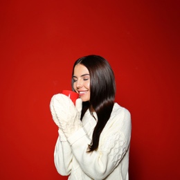 Young woman in warm sweater with cup of hot drink on red background