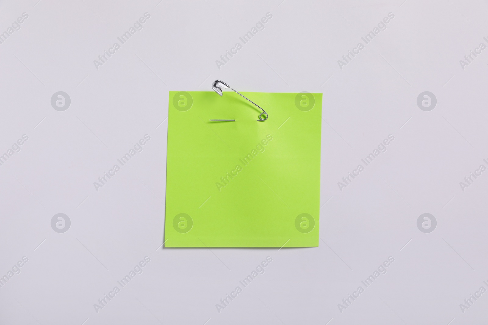 Photo of Light green paper note attached with safety pin to white background, top view