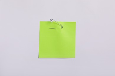 Photo of Light green paper note attached with safety pin to white background, top view