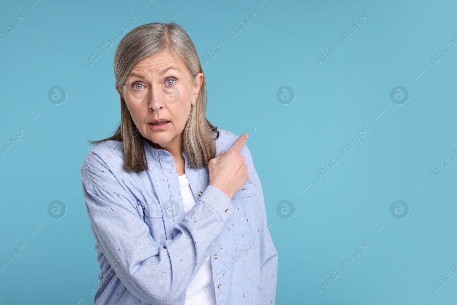 Photo of Surprised senior woman pointing at something on light blue background, space for text