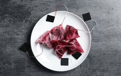 Photo of Saucer with used pyramid tea bags on grey table, top view