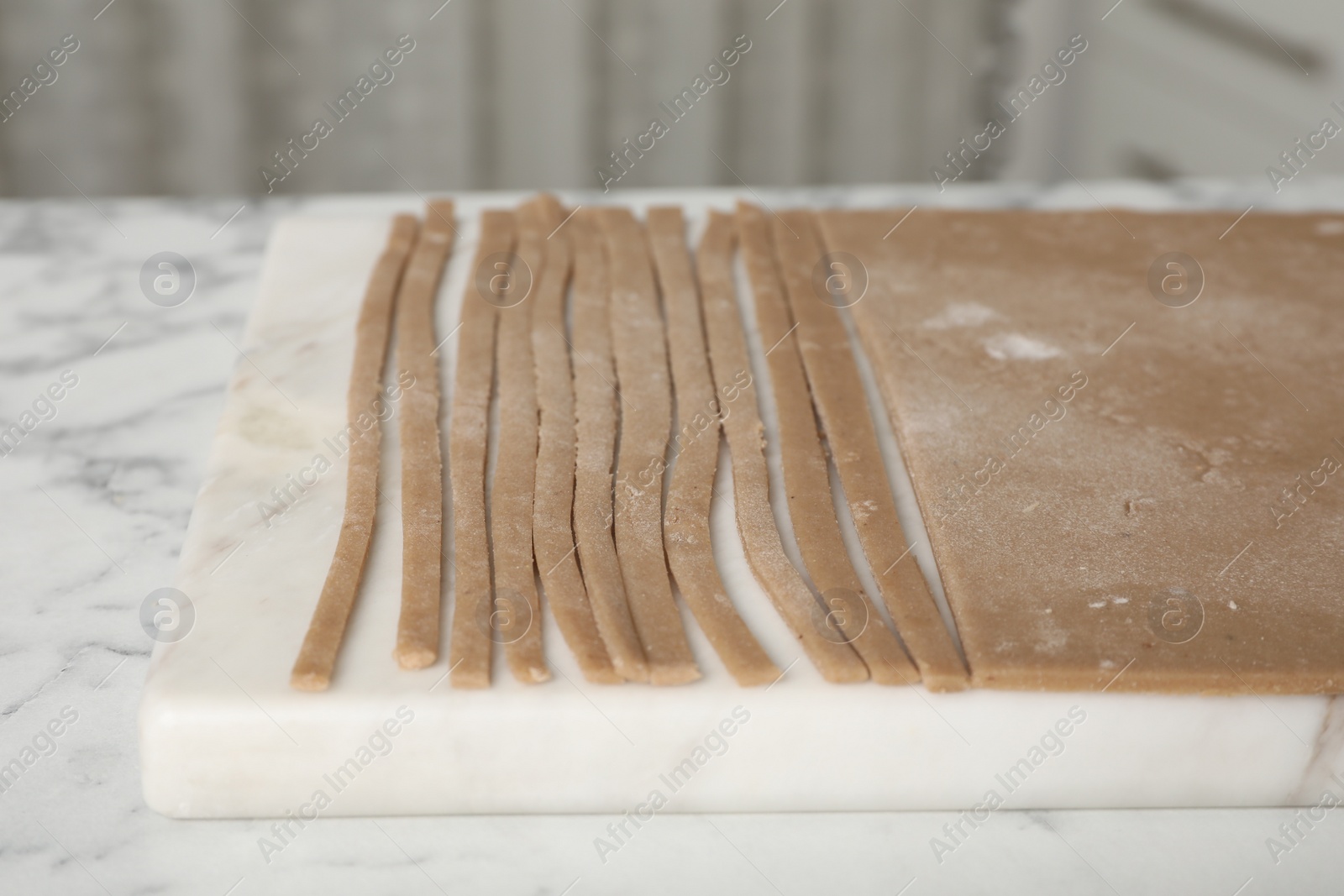 Photo of Making homemade soba (buckwheat noodles) on white marble table indoors, closeup