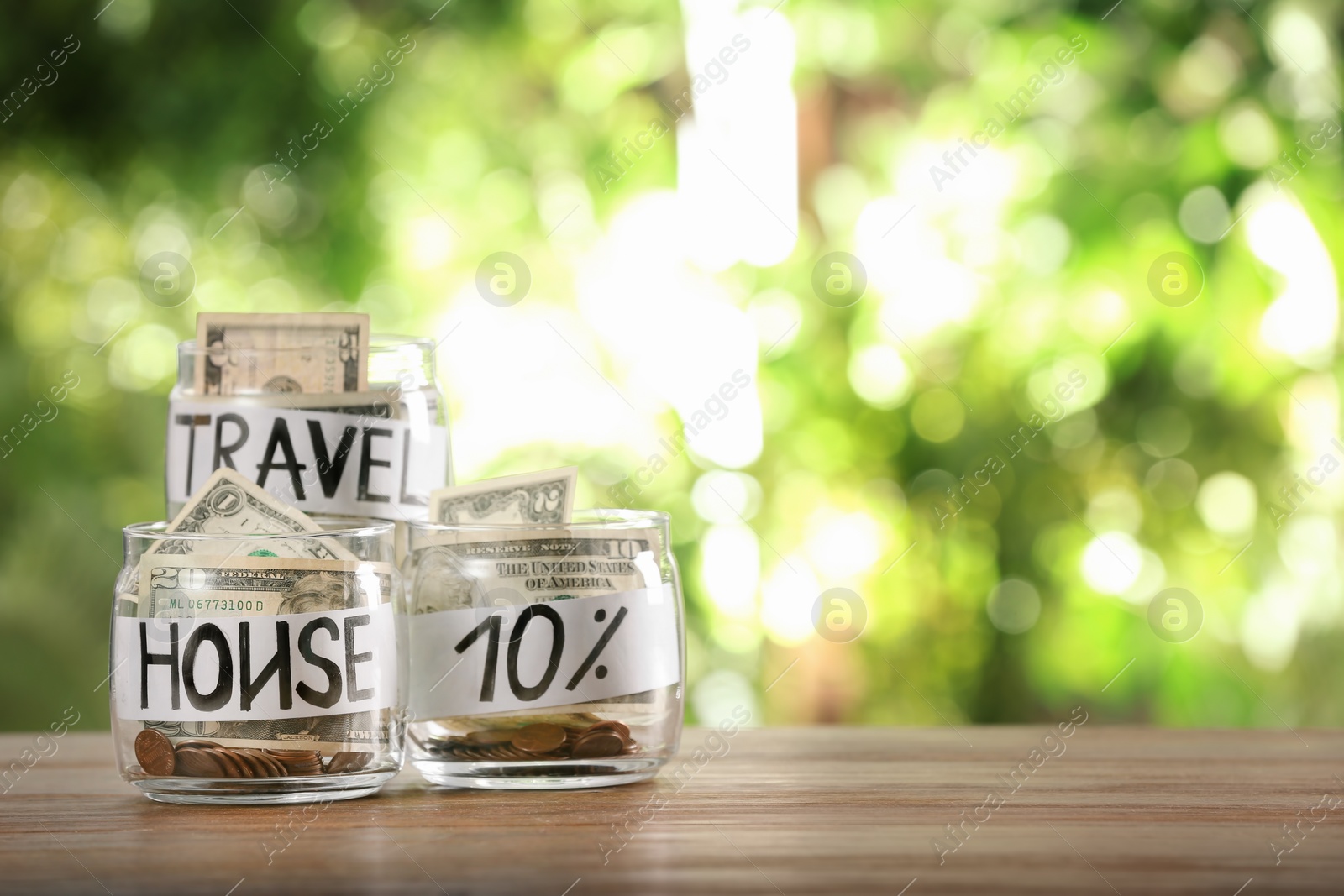 Photo of Glass jars with money for different needs on table against blurred background, space for text