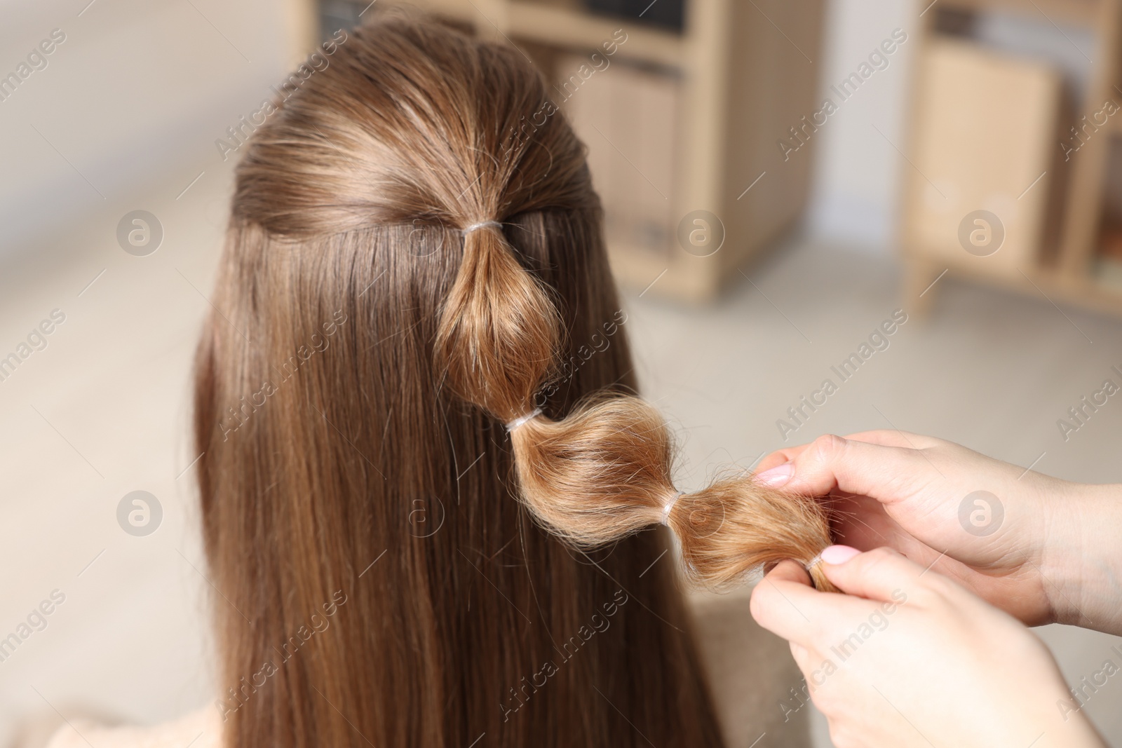 Photo of Professional stylist braiding woman's hair indoors, closeup