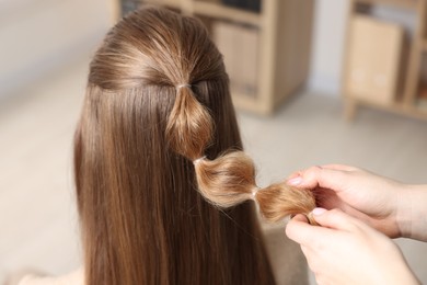 Professional stylist braiding woman's hair indoors, closeup