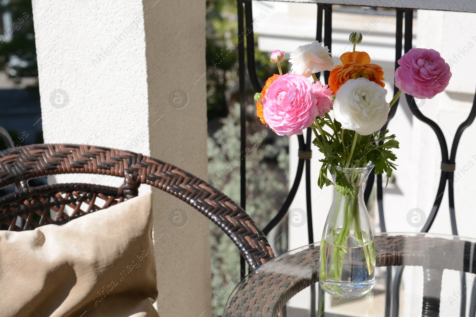 Photo of Bouquet of beautiful bright ranunculus flowers in glass vase on table at balcony
