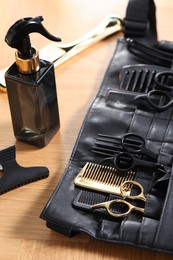 Hairdresser tools. Professional scissors and combs in leather organizer on wooden table, closeup