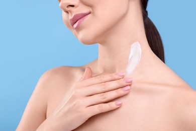 Woman with smear of body cream on her neck against light blue background, closeup