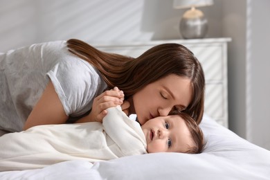 Happy mother kissing her little baby on bed at home