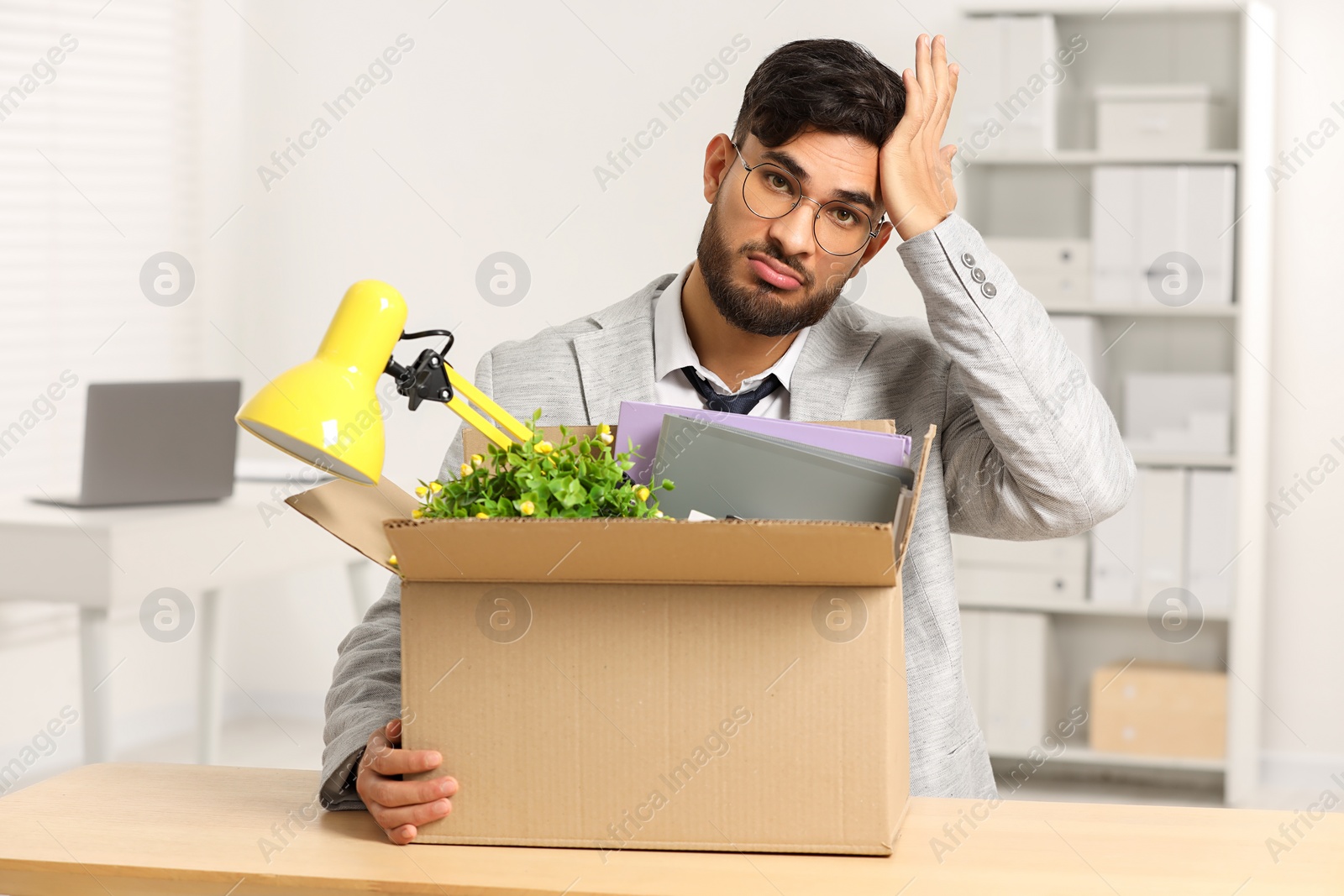 Photo of Unemployment problem. Frustrated man with box of personal belongings at desk in office