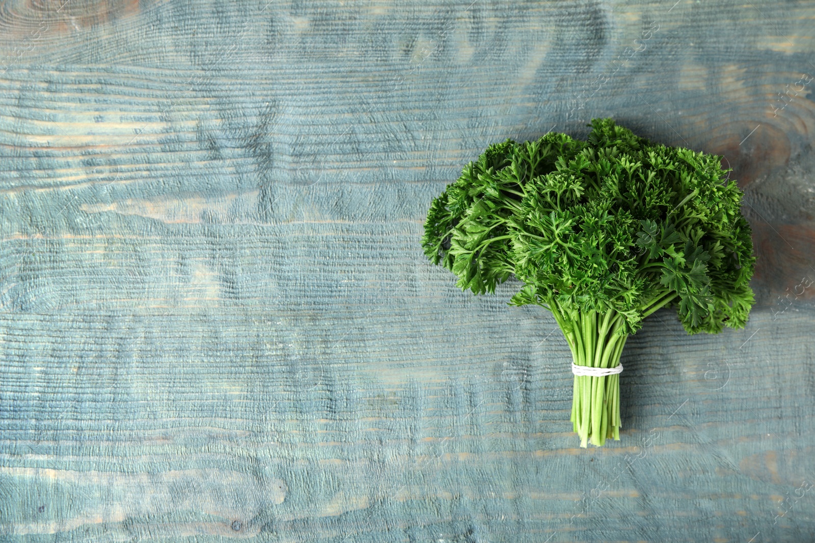 Photo of Bunch of fresh green parsley on blue wooden background, top view. Space for text