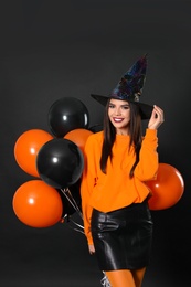 Photo of Beautiful woman wearing witch costume with balloons for Halloween party on black background