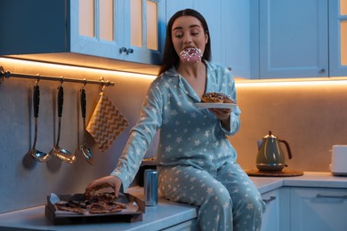 Photo of Young woman eating junk food in kitchen at night. Bad habit
