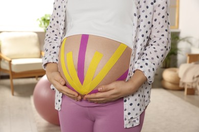 Pregnant woman with kinesio tapes on her belly at home, closeup