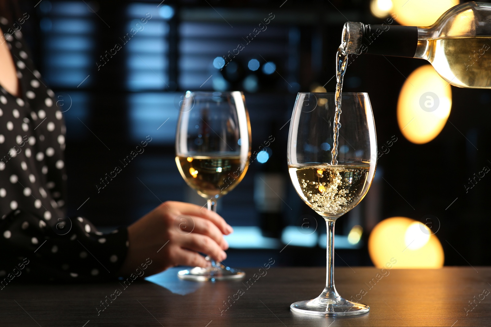 Photo of Pouring white wine from bottle into glass on bar counter