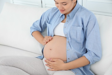 Photo of Beautiful pregnant woman sitting on sofa at home, closeup