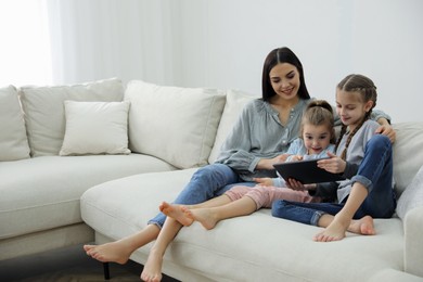 Photo of Mother and daughters with tablet sitting on comfortable sofa in living room