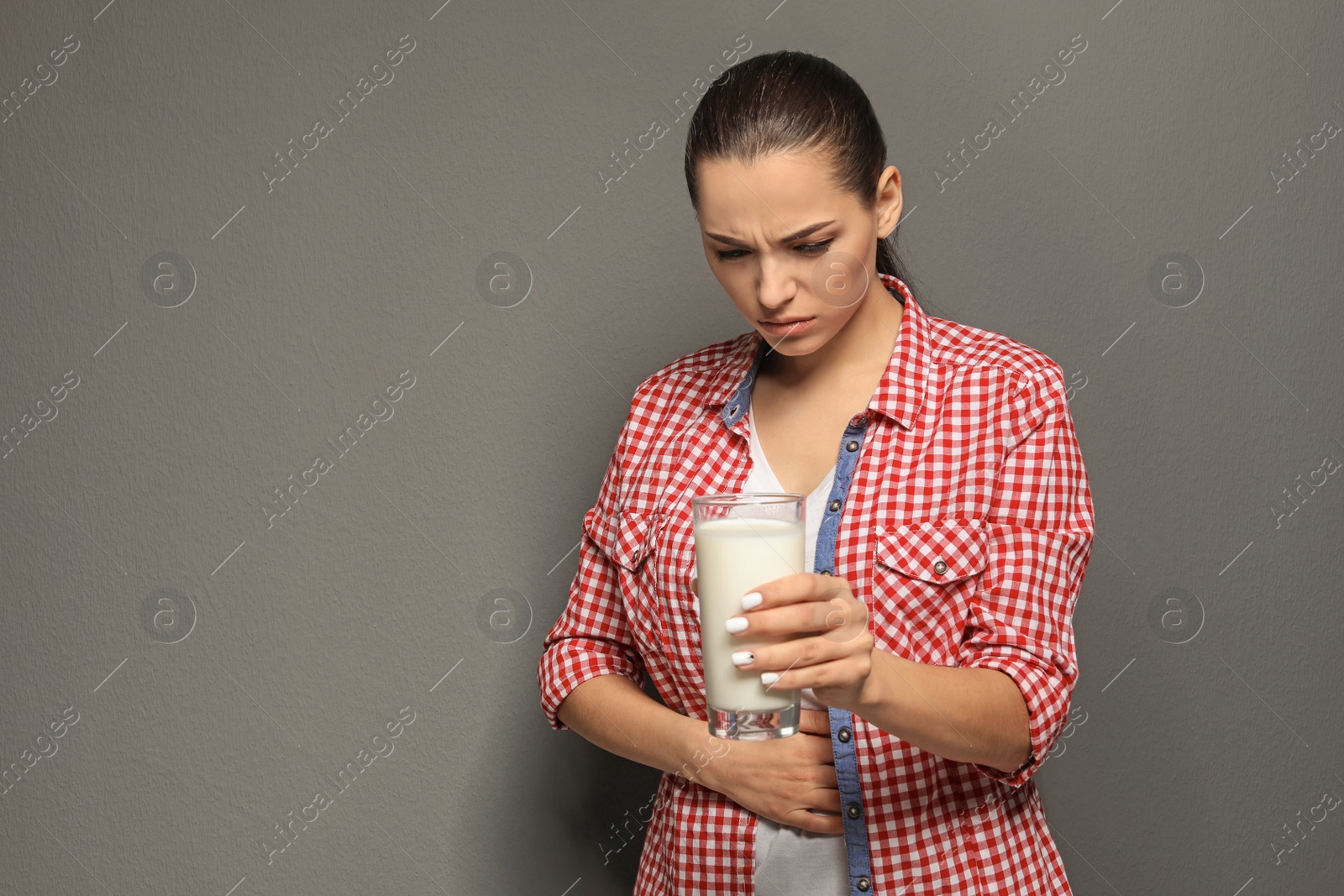Photo of Young woman with dairy allergy holding glass of milk on grey background