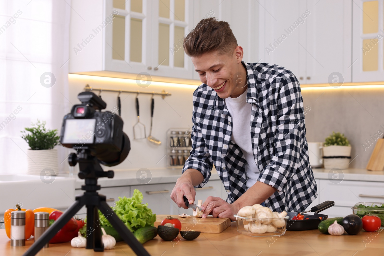 Photo of Smiling food blogger cooking while recording video in kitchen