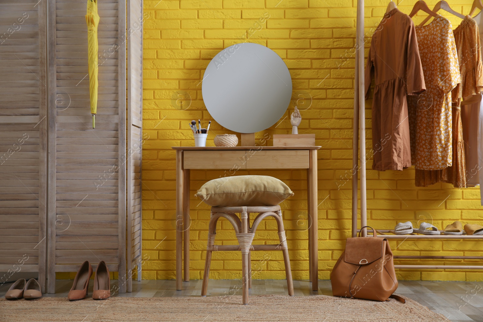 Photo of Wooden stool, dressing table and rack with clothes near yellow brick wall indoors