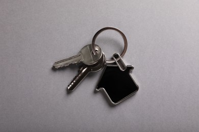 Photo of Keys with trinket in shape of house on grey background, top view. Real estate agent services