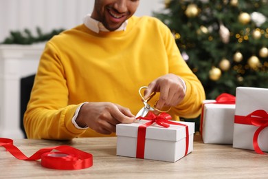 Photo of Man decorating Christmas gift box at wooden table in room, closeup