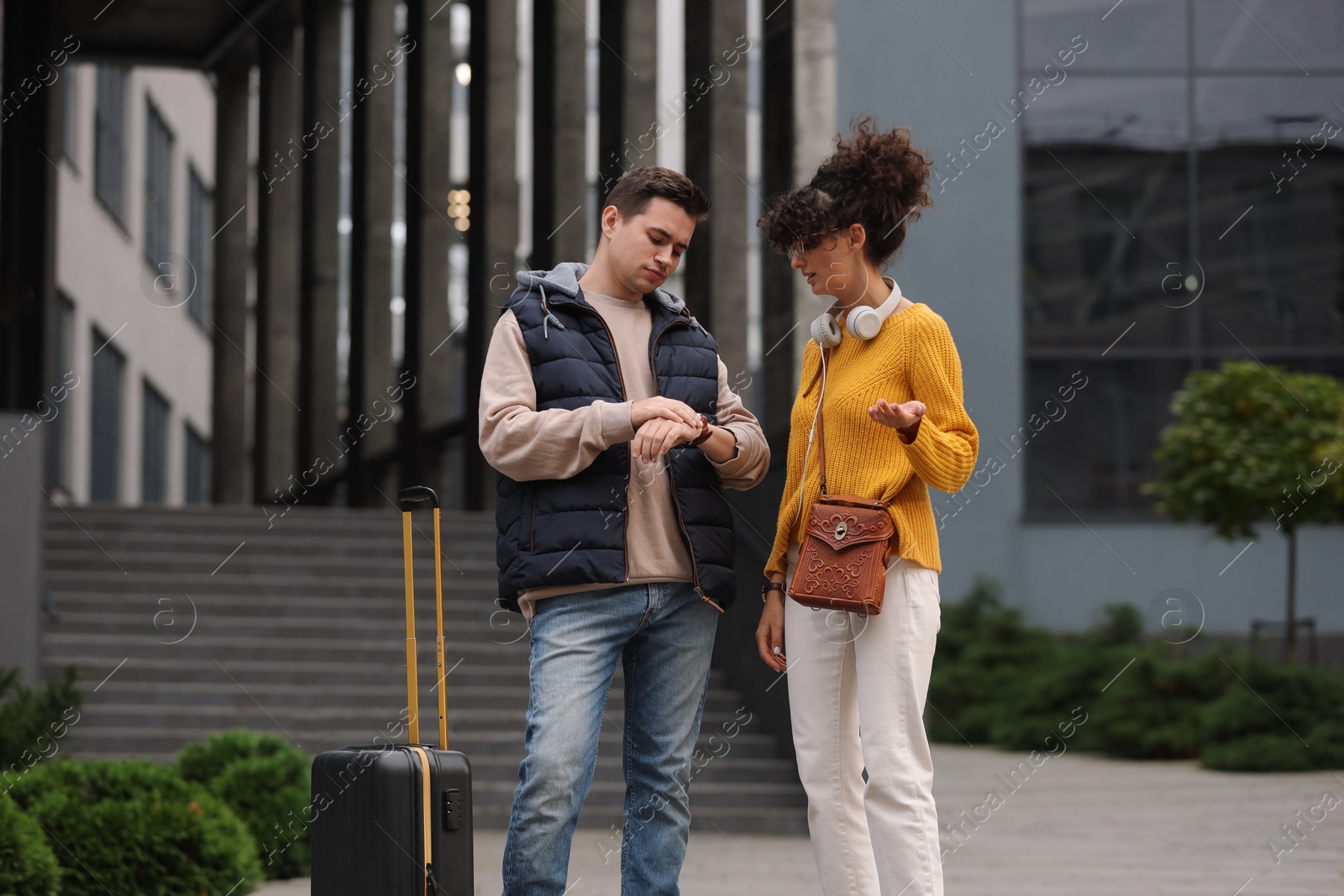 Photo of Being late. Worried couple with suitcase looking at watch outdoors