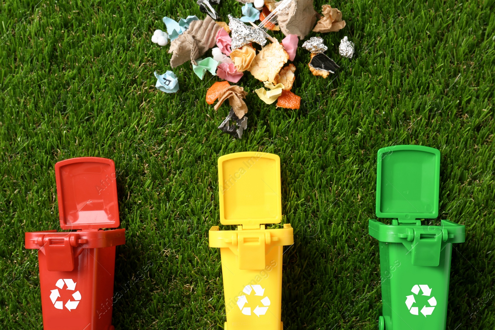 Photo of Trash bins and different garbage on green grass, top view. Waste recycling concept