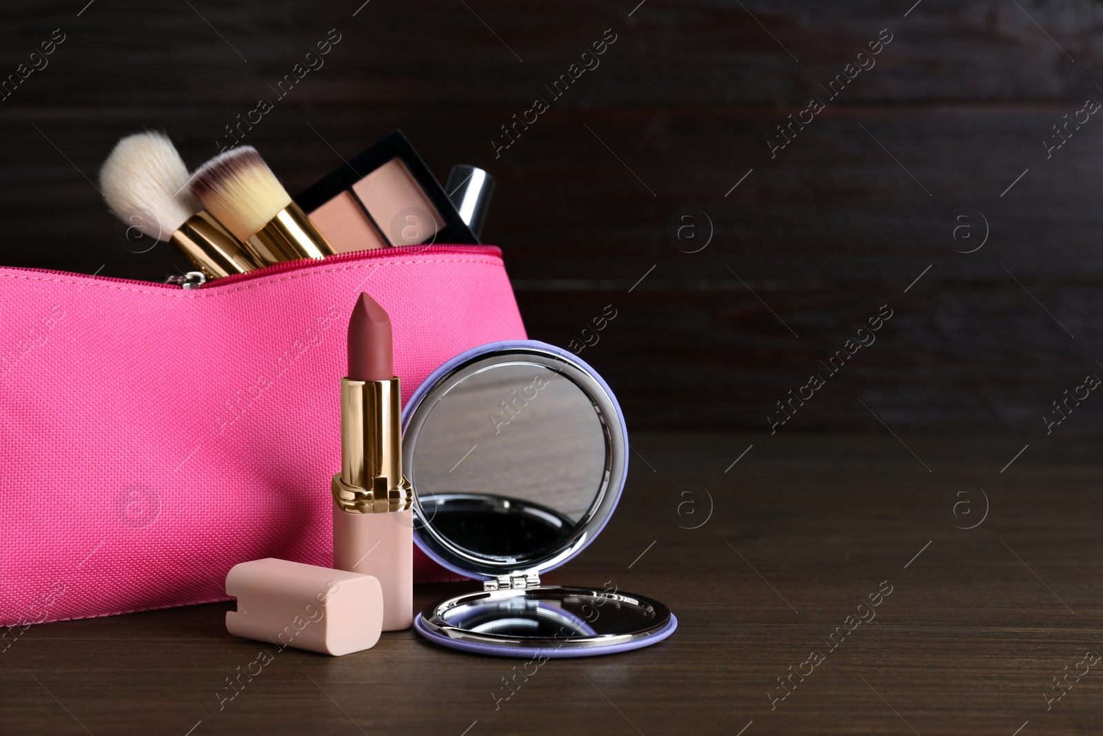 Photo of Stylish pocket mirror and cosmetic bag with makeup products on wooden table, space for text