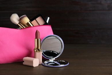 Photo of Stylish pocket mirror and cosmetic bag with makeup products on wooden table, space for text