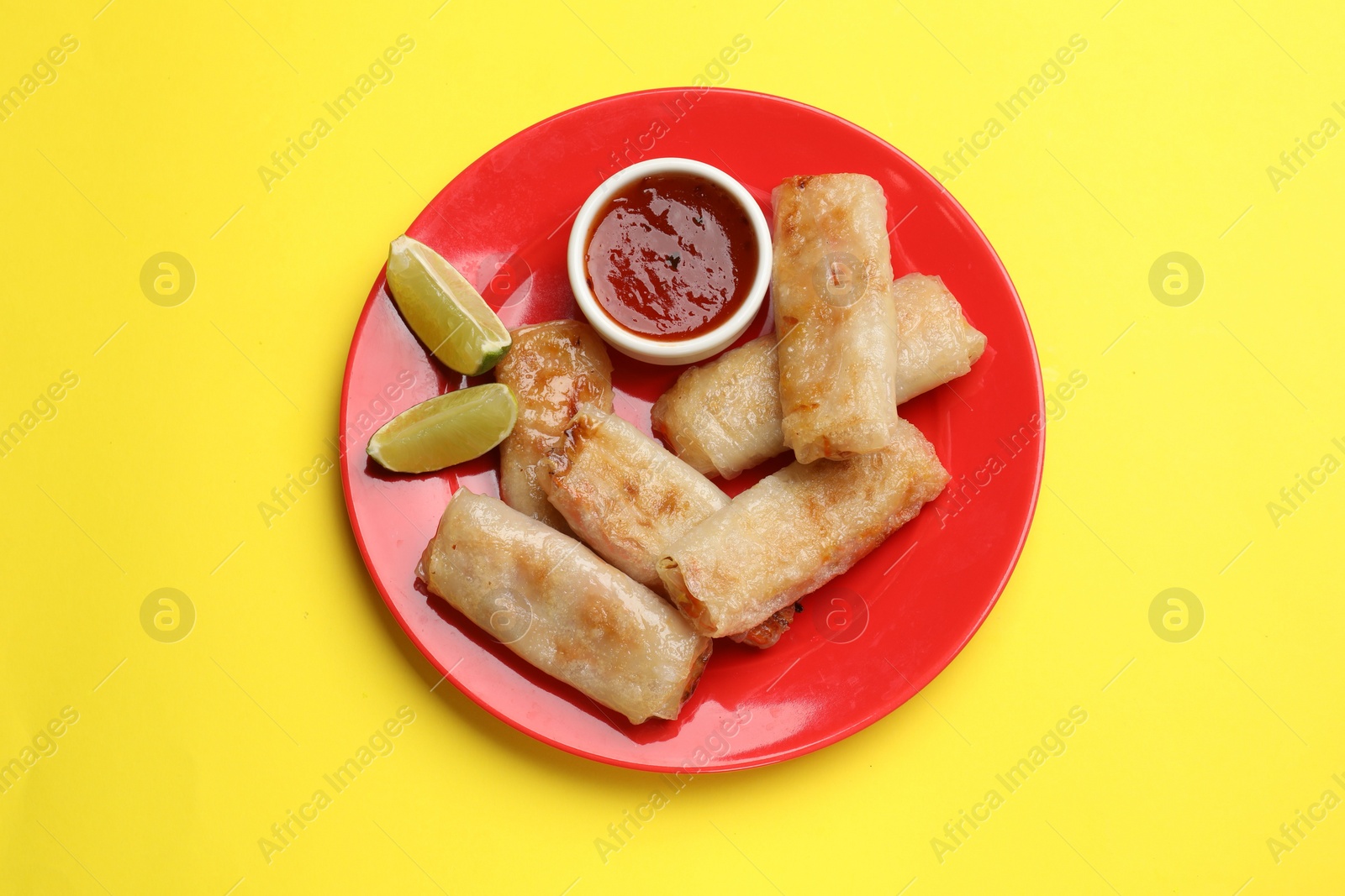 Photo of Tasty fried spring rolls, lime and sauce on yellow table, top view