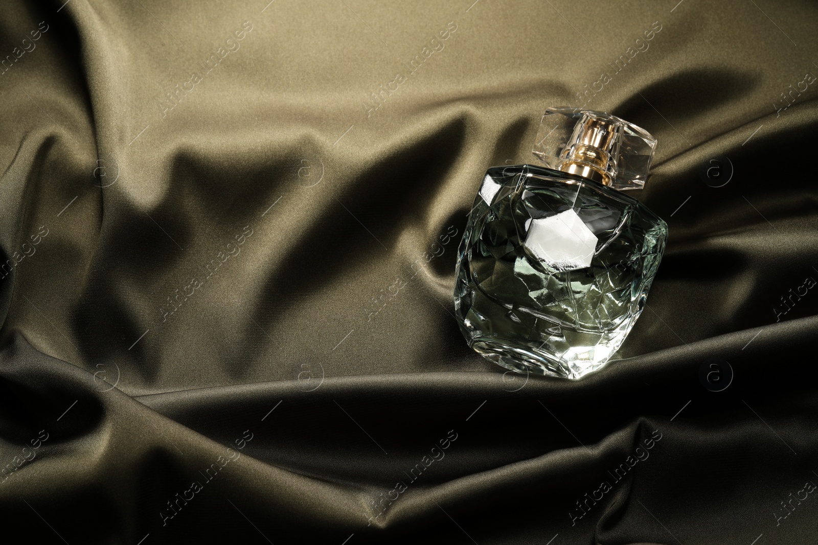 Photo of Luxury perfume in bottle on dark silk fabric, top view