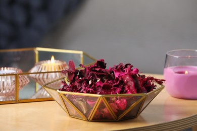 Photo of Aromatic potpourri of dried flowers in bowl and burning candles on table indoors