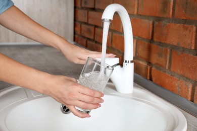 Woman filling glass with water from faucet in kitchen, closeup