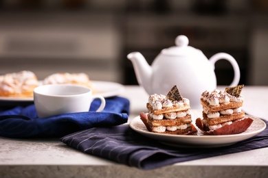 Photo of Plate with tasty pastries, teapot and cup on table