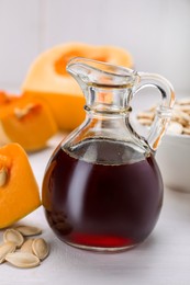 Fresh pumpkin seed oil in glass jug on white wooden table