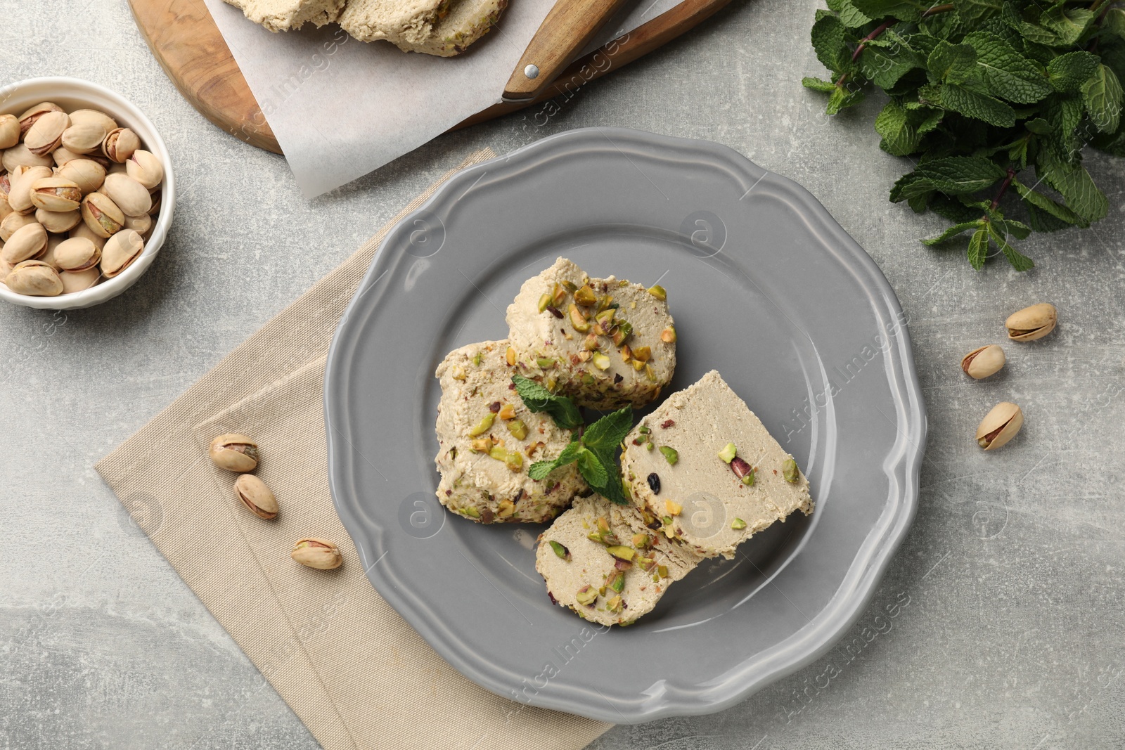 Photo of Tasty halva with pistachios and mint on light grey table, flat lay