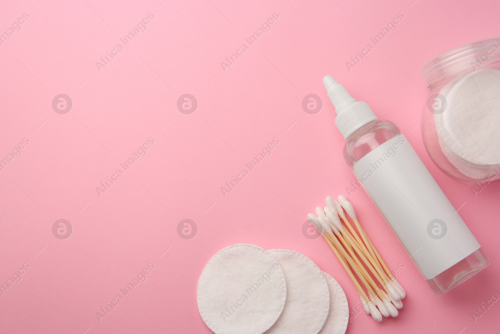 Photo of Bottle of makeup remover, cotton pads and swabs on pink background, flat lay. Space for text