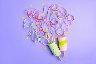Beautiful serpentine and confetti bursting out of party poppers on violet background, flat lay