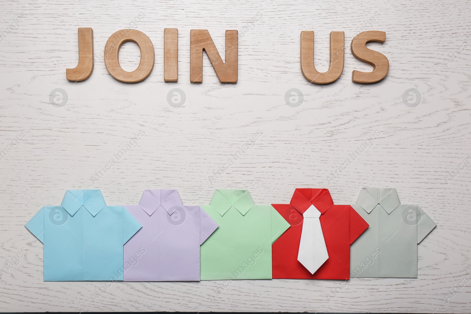 Photo of Many paper shirts and phrase Join Us on white wooden background, flat lay. Recruiter searching employee