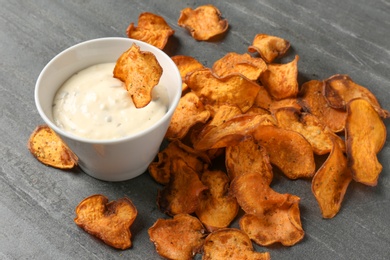 Photo of Sweet potato chips and bowl of sauce on grey background