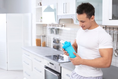 Photo of Man with bottle of protein shake in kitchen. Space for text